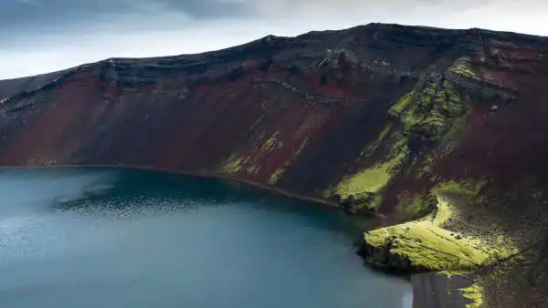 A blue crater lake with red mountain surrounding it